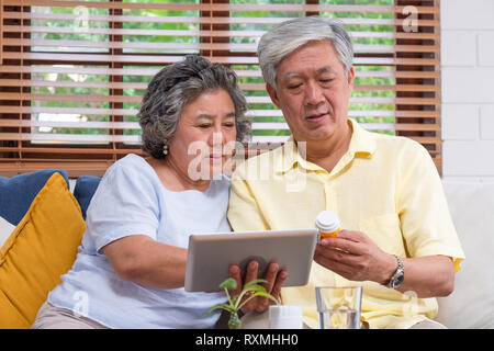 Asiatische senior Paar verwenden Tablet suche Verschreibung der Pille, während auf dem Sofa zu Hause sitzen, Senior lernen Technologie zu verwenden. Das Altern zu Hause. Stockfoto