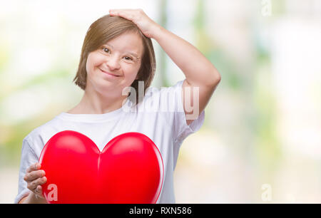 Junge erwachsene Frau mit Down Syndrom halten roten Herzen über isolierte Hintergrund mit Hand betonte am Kopf, schockiert mit Scham und Überraschung Gesicht, Angr Stockfoto