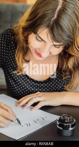 Kalligraph junge Frau schreibt Phrase auf weißem Papier. Bibel Phrase über die Liebe einschreibt ornamental verzierten Buchstaben. Kalligrafie, Grafik Design Stockfoto