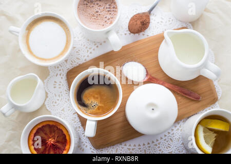 Kaffee, Cappuccino, Kakao und Tee auf einem weißen Tisch mit einem Holzbrett und Kerzen. Ansicht von oben, flach Stockfoto