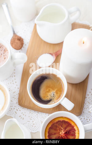Kaffee, Cappuccino, Kakao und Tee auf einem weißen Tisch mit einem Holzbrett und Kerzen Stockfoto