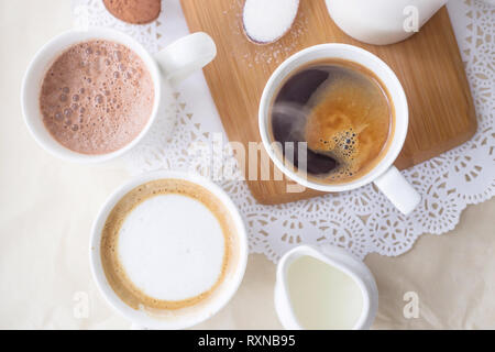 Kaffee, Cappuccino, Kakao und Tee auf einem weißen Tisch mit einem Holzbrett und Kerzen. Ansicht von oben, flach Stockfoto