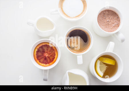 Kaffee, Cappuccino, Kakao und Tee auf einem weißen Tisch in minimalistisch-Cups. Ansicht von oben, flach Stockfoto
