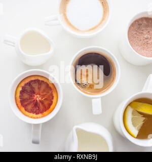 Kaffee, Cappuccino, Kakao und Tee auf einem weißen Tisch in minimalistisch-Cups. Ansicht von oben, flach Stockfoto