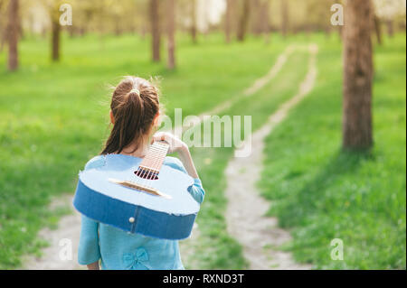 Konzept der vagrant junge Musiker kleines Mädchen walking outdoor Spring Park entlang der akustischen Spanisch denim Gitarre auf ihrer Schulter Stockfoto