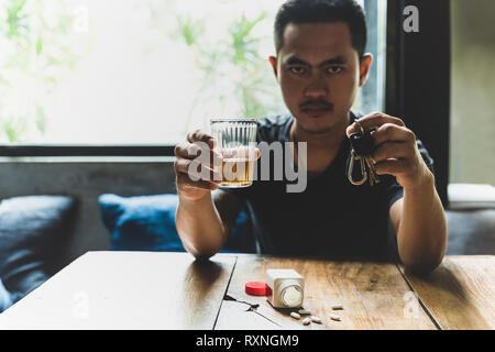 Mann hält ein Glas Whiskey und Autoschlüssel mit Pillen auf den Tisch. Stockfoto