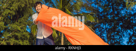 Sommer lifestyle Portrait von Mensch bläst einem aufblasbaren Orange Sofa am Strand von tropischen Insel. Entspannen und genießen das Leben auf der Luft Bett BANNER Stockfoto