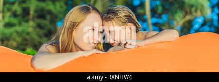 Sommer lifestyle Portrait von Mutter und Sohn sitzen auf dem Orange aufblasbare Sofa auf den Strand von tropischen Insel. Entspannen und genießen das Leben auf der Luft Stockfoto