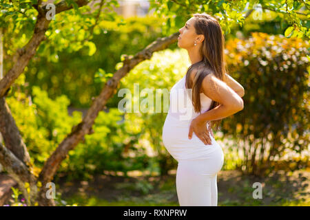 Erschöpft schwangere Frau im Garten, Hände auf dem Rücken Stockfoto