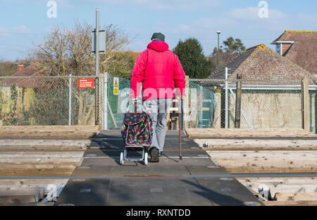 Person ziehen Einkaufswagen über einen Fußgänger Bahnübergang bei Ferring, West Sussex, England, UK. Stockfoto