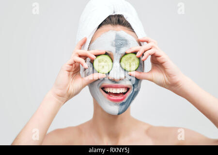 Junge Frau in Handtuch mit Clay Mask holding Scheiben Gurke gegen ihre Augen Stockfoto