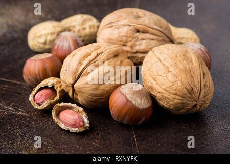 Haufen Nüsse in der Schale, und auf einem dunklen Hintergrund geschält. Walnüsse, Haselnüsse, Erdnüsse. Lecker gesunde Snack, Essen Stockfoto