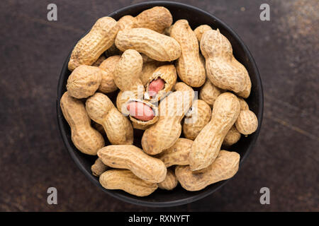 Erdnüsse in der Schale Schüssel auf dunklem Hintergrund. Gesundes Essen, ganze unbehandelte Nüsse, leckeren Snack Stockfoto