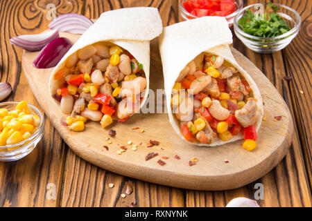 Burrito in tartilla mit Fleisch, Gemüse, weiße Bohnen, Paprika, Mais. Ein leckeres Mittagessen, mexikanische Küche, hausgemachte Snacks Stockfoto