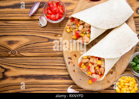 Burrito in tartilla mit Fleisch, Gemüse, weiße Bohnen, Paprika, Mais. Ein leckeres Mittagessen, mexikanische Küche, hausgemachte Snacks Stockfoto