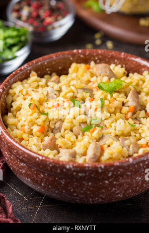 Bulgur mit der Türkei, Schwein oder Rind. Östlichen Reisgericht mit köstlichen Speisen. Geschmortes Fleisch mit Grütze. Pilav auf dunklem Hintergrund Stockfoto