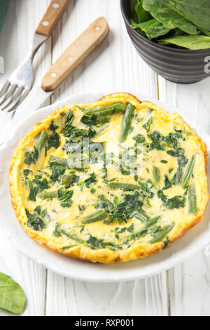 Omelette mit Spinat und grünen Bohnen, gesundes Essen. Ei und Milch Frittata, leckeres Frühstück auf weißem Holz- Hintergrund Stockfoto