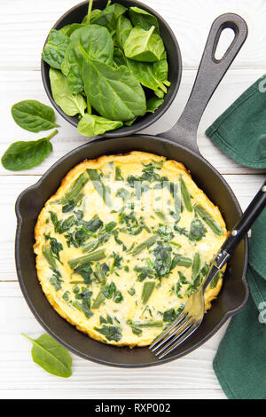 Omelette mit Spinat und grünen Bohnen, gesundes Essen. Ei und Milch Frittata, leckeres Frühstück. In schwarz Bratpfanne auf weißem Holz- Hintergrund Stockfoto