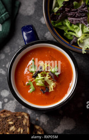 Rote Gemüse Cremesuppe in Blau Becher (Tomaten, Karotten, Linsen, Kürbis), köstlichen warmen hausgemachten Mittagessen in Schale. Dunkler Hintergrund Stockfoto