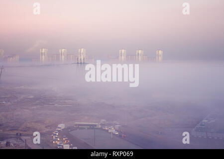 Morgennebel deckt die Fabrik und electrotowers. Ungewöhnliche Landschaft. Autos im Nebel Stockfoto