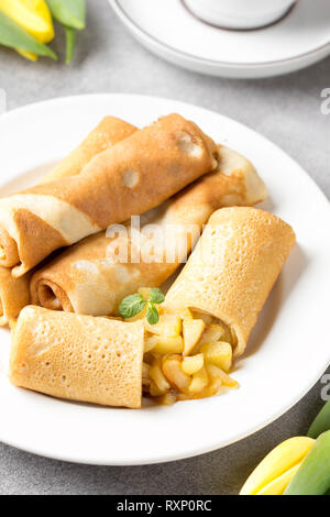 Dünne Palatschinken (Pfannkuchen) mit Apple füllen, gefüllte Brötchen, Russische traditionelle Lebensmittel für die maslenitsa, französischer Nachtisch, Frühstück mit Tulpen auf Mutter d Stockfoto