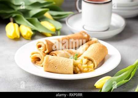 Dünne Palatschinken (Pfannkuchen) mit Apple füllen, gefüllte Brötchen, Russische traditionelle Lebensmittel für die maslenitsa, französischer Nachtisch, Frühstück mit Tulpen auf Mutter d Stockfoto