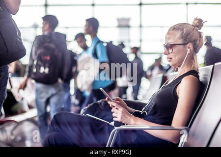 Weibliche Reisende können Sie über Ihr Handy während der Wartezeit in ein Flugzeug steigen bei der Abreise Gates in asiatischen Flughafen Terminal. Stockfoto