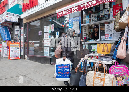 Eine Straßenszene in Jackson Heights in Queens, New York, mit einer Frau Einkaufen für Pocket Bücher an einer im Stehen auf 74th Street. Stockfoto