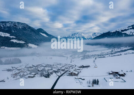 Morgen neblig top Antenne Panoramablick auf Schnee und Dorf mit Bäumen und Straße auf der Winter Landschaft Hintergrund der österreichischen Alpen, Ski Res Stockfoto