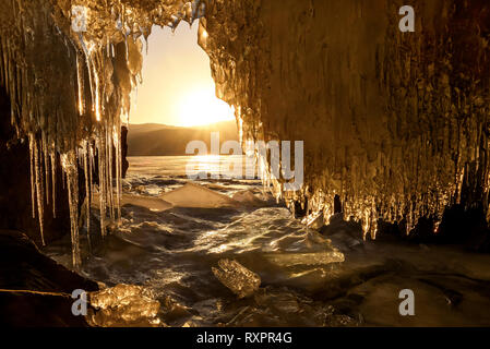 Erstaunlich Sonnenaufgang über den Bergen und der zugefrorene See im Winter aus dem Eis Höhle mit Eiszapfen. Teletskoye See, Altai, Russland Stockfoto