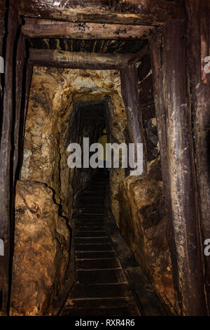 Alter Bergwerkstollen mit hölzernen Holzausbau und Person gekleidet in einem Bergbau Mantel im Hintergrund Stockfoto