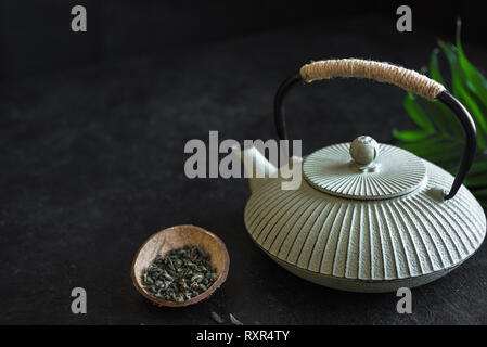 Asiatische Teekanne und Kaffee auf schwarzem Hintergrund, kopieren. Traditionelle asiatische Anordnung für Tee Zeremonie - Eisen Teekanne und trockenen grünen Tee. Stockfoto
