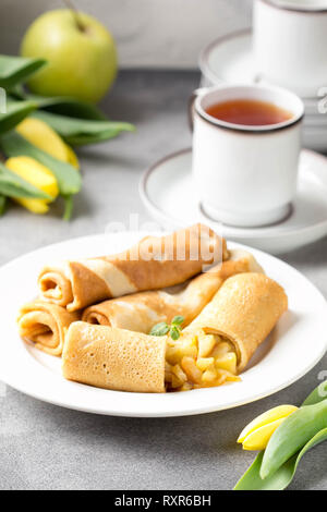 Dünne Palatschinken (Pfannkuchen) mit Apple füllen, gefüllte Brötchen, Russische traditionelle Lebensmittel für die maslenitsa, französischer Nachtisch, Frühstück mit Tulpen auf Mutter d Stockfoto