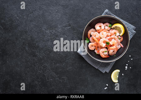 Garnelen in der Schüssel, Ansicht von oben, kopieren. Frische Meeresfrüchte Hintergrund - Garnelen Schwänze auf Schwarz. Gekochte Garnelen. Stockfoto