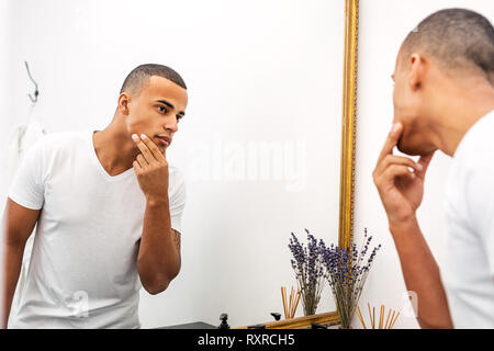 Porträt von einem gutaussehenden jungen Mann sein Gesicht Prüfung im Badezimmerspiegel Stockfoto