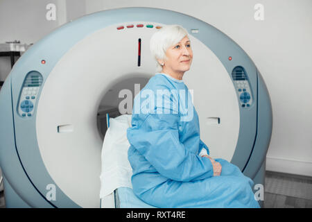 Nachdenklich, ältere Frau sitzt auf der scanner Tabelle. Warten auf CT-Scan Stockfoto