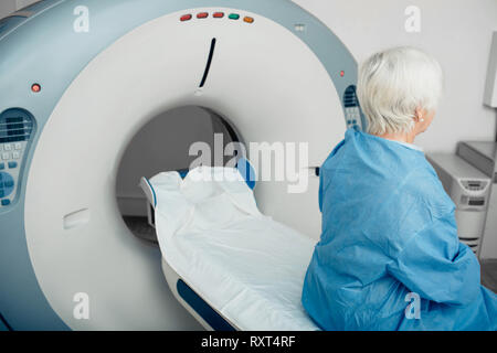 Nachdenklich, ältere Frau sitzt auf der scanner Tabelle. Warten auf CT-Scan Stockfoto