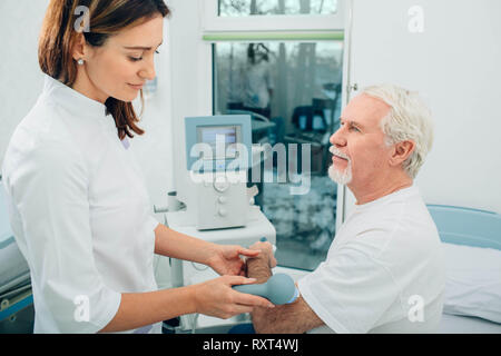 Physiotherapeut mit Ultraschall Maschine an Hand von Client in der Klinik. Physiotherapeutische Behandlung Stockfoto