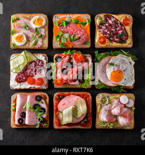 Satz von acht verschiedenen Sandwiches mit Fleisch in quadratische Form. Top View oder flach. Sortiment Fleisch Toast auf schwarzem Hintergrund. Idee, kreatives Konzept für wurstmacher Stockfoto