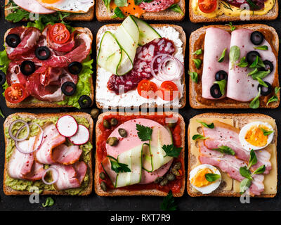 Satz von acht verschiedenen Sandwiches mit Fleisch in quadratische Form. Top View oder flach. Sortiment Fleisch Toast auf schwarzem Hintergrund. Idee, kreatives Konzept für wurstmacher Stockfoto