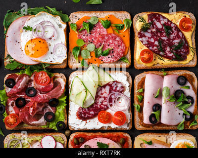 Satz von acht verschiedenen Sandwiches mit Fleisch in quadratische Form. Top View oder flach. Sortiment Fleisch Toast auf schwarzem Hintergrund. Idee, kreatives Konzept für wurstmacher Stockfoto