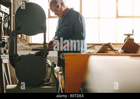 Ältere Arbeitnehmer arbeiten an bandsäge Maschine in seiner Werkstatt. Tischler Schneiden von Holz auf der Maschine in der Schreinerei. Stockfoto