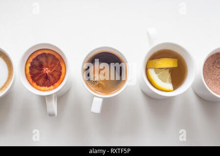 Warme Getränke Kaffee und Tee in Weiß Cups stehen in einer Linie auf einem weißen Tisch. Ansicht von oben, flach Stockfoto