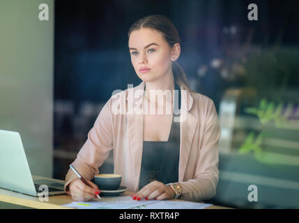 Elegante business Frau suchen durch das Fenster in ein Cafe Shop. Nachdenklich. Selektiver Fokus und Reflexion über das Fenster Stockfoto