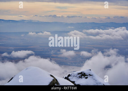 Blick über den Winter in großer Höhe von schneebedeckten Felsen über den Wolken in Richtung der fernen Ebenen, Hohen Tatra, Slowakei. Stockfoto
