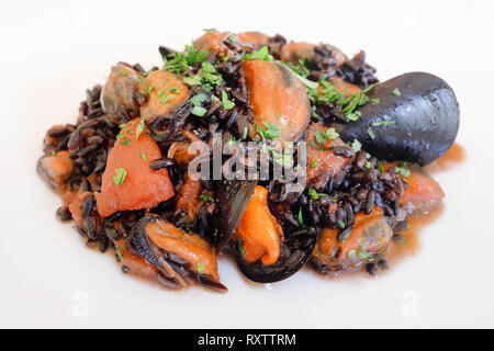 Miesmuscheln mit schwarzer Reis, mit gehackten Tomaten, Olivenöl, Knoblauch, Gewürze und Petersilie gekocht. Fisch essen fertig zu essen. Close-up Stockfoto