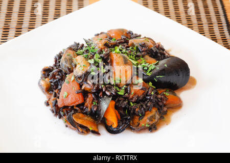 Miesmuscheln mit schwarzer Reis, mit gehackten Tomaten, Olivenöl, Knoblauch, Gewürze und Petersilie gekocht. Fisch essen fertig zu essen. Close-up Stockfoto