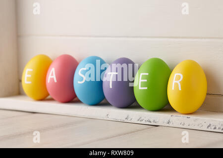 Bunt bemalte Eier mit Buchstaben in einem Wort Ostern auf weißem Holzbohlen Hintergrund angeordnet. Urlaub Konzept. Stockfoto