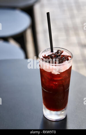 Red Cocktail mit einem schwarzen Stroh auf die dunkle runde Tisch im Café draußen auf den verschwommenen Hintergrund. Closeup vertikale Foto. Stockfoto
