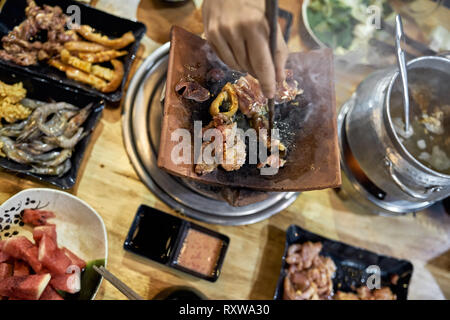 Männliche Hand mit Stäbchen ist Kochen Stücke vom Huhn auf den heißen Topf in der traditionellen lokalen Cafe in Vietnam. Abwechslungsreiches Essen auf dem Teller und Schalen ar Stockfoto